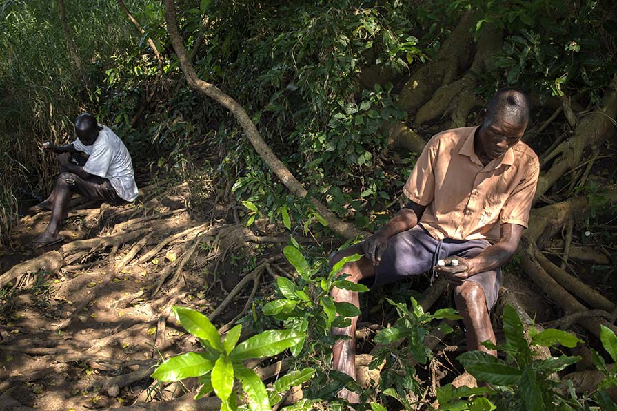 Two men sit beside a river.